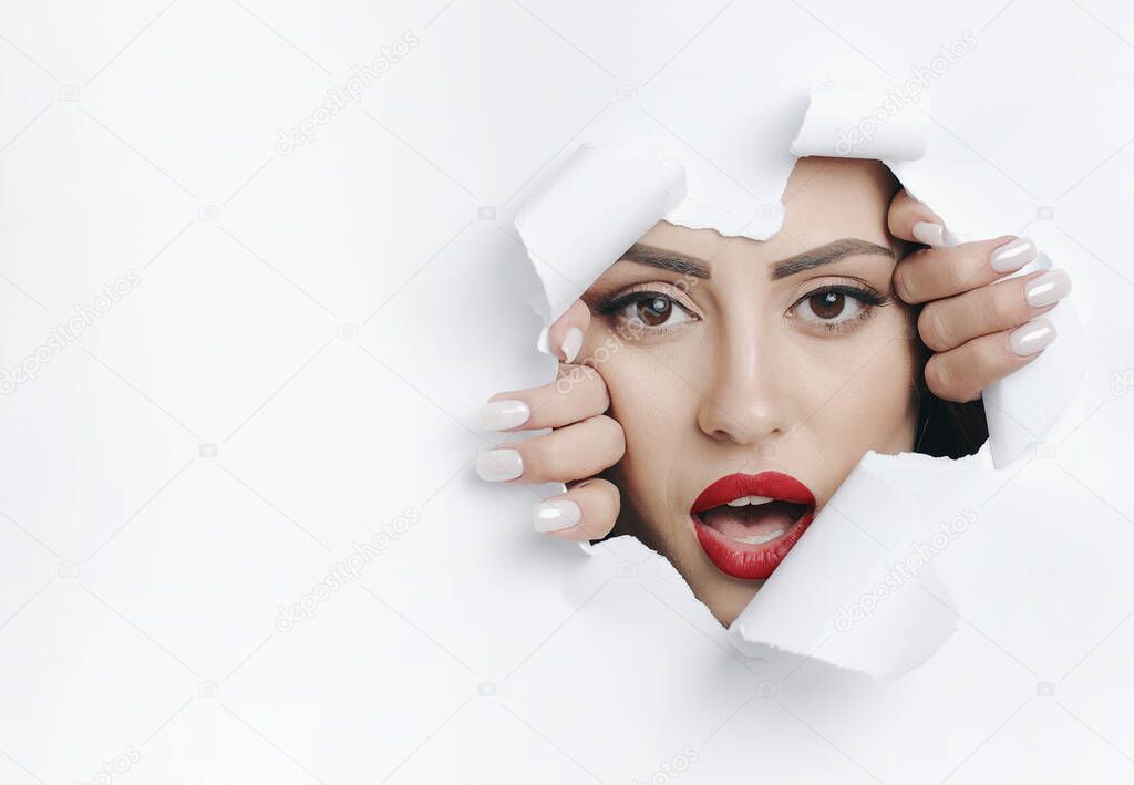 Young Woman Looking Through a Hole in White Wall
