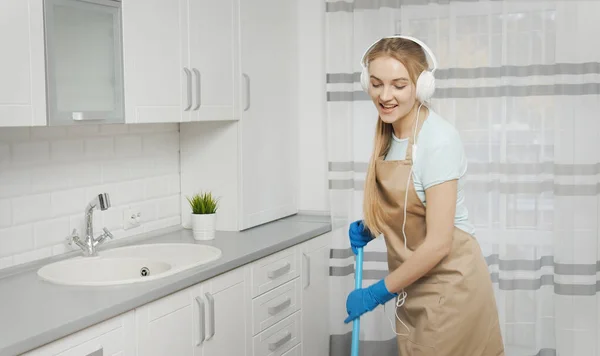 Chica escuchando la música mientras cepilla piso de la cocina Imagen de stock