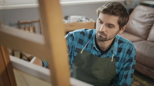 Joven artista guapo serio mirando críticamente un lienzo Imagen de stock