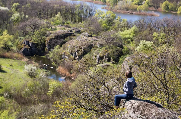 Hembra caucásica sentada en una gran piedra sobre el río y el bosque, en primavera — Foto de Stock