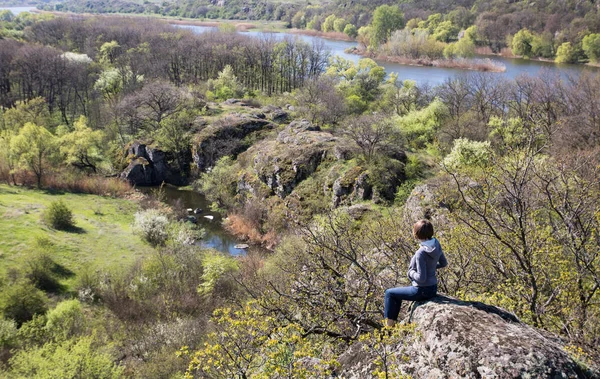 Mujer caucásica sentada en una gran piedra sobre el río y el bosque, en primavera. pequeña isla en el río —  Fotos de Stock