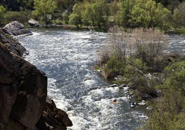 stream of the river, white water with rapids, rock on the foreground, two kayaks in the water