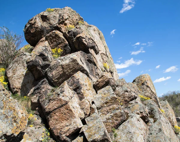 Zbliżenie kaskadowe kamieni na skale, Błękitne niebo na tle, żółte kwiaty między kamieniami, orientacja pionowa — Zdjęcie stockowe