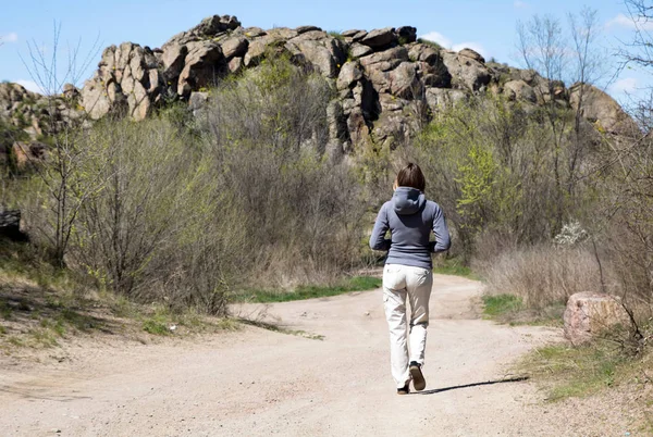 Une randonneuse se dirige vers les rochers. Route blanche, buissons et arbres, printemps — Photo