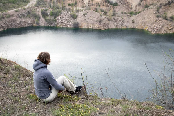 大きな石 abobe の青い湖に座っている女の子。ほとりの岩ガレ場。彼女の足を抱擁します。 — ストック写真