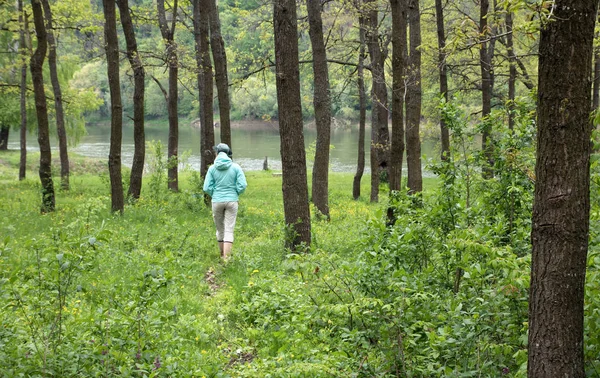 Femelle en bottes de caoutchouc et chapeau vert marche par le chemin dans la forêt caduque verte à la rivière — Photo