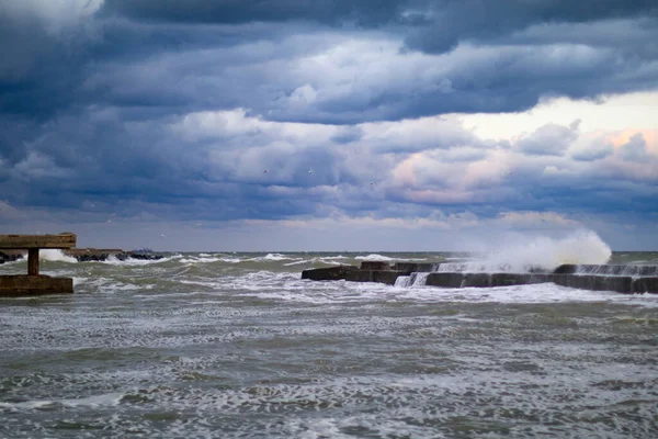 blue stormy clouds, storm at sea, waves are breaking of the pier, dirty orange water