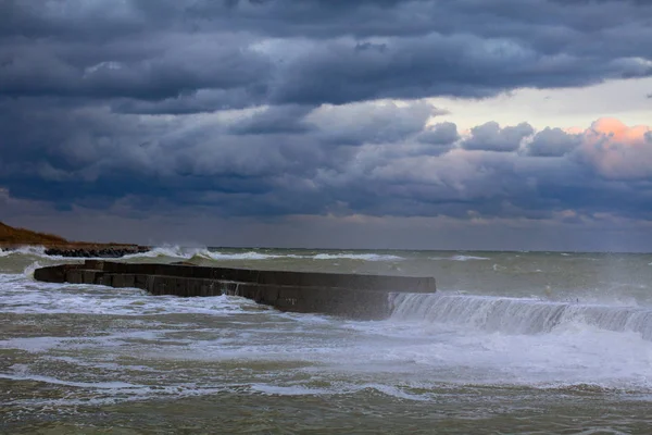 Голубые грозовые облака, шторм в море, волны ломаются от причала, грязная оранжевая вода — стоковое фото