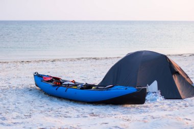Gün batımında deniz kenarında bir çadırın yanında kano.