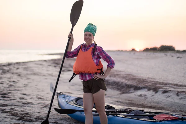 Jeune femme avec pagaie près de l'expédition kayak sur la plage au coucher du soleil — Photo