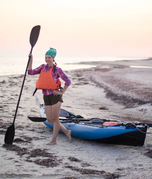 Jeune femme avec pagaie près de l'expédition kayak sur la plage au coucher du soleil — Photo