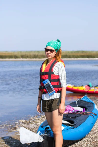 Fille aux cheveux roux en gilet de sauvetage rouge préparant pour l'expédition sur des kayaks — Photo