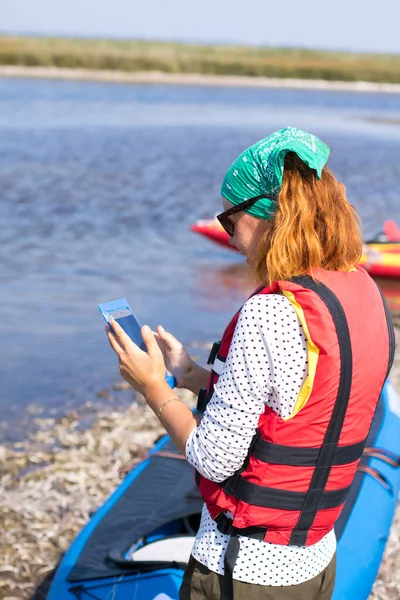 Chica pelirroja en chaleco salvavidas rojo tomar fotos en el teléfono inteligente — Foto de Stock