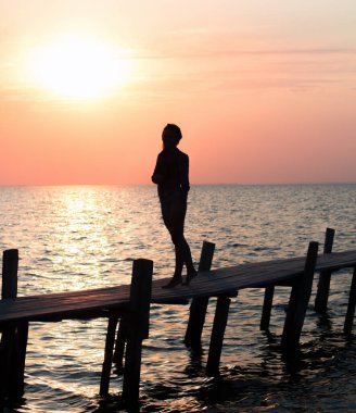 Gün batımında, sahilde, ahşap ranzadaki kızın silueti.