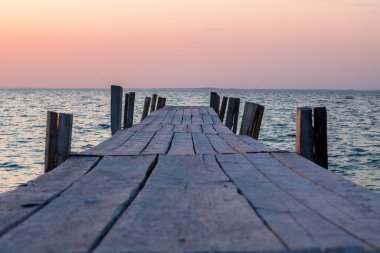 Eski tahtalardan ahşap döşeme günbatımında denize açılıyor.