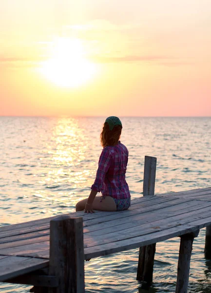 Het meisje zit op de oude houten ligplaats en bewondert zonsondergang op zee — Stockfoto