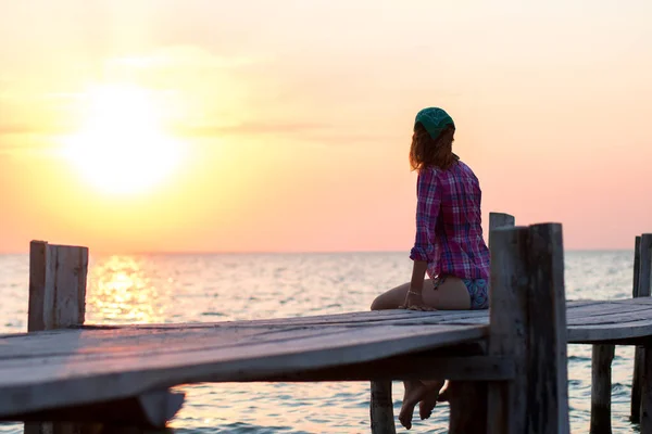 Девушка сидит на старом деревянном причале и любуется закатом моря — стоковое фото