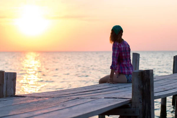 Het meisje zit op de oude houten ligplaats en bewondert zonsondergang op zee — Stockfoto