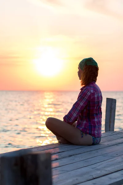 Meisje doet yoga asana op een oude houten pier en geniet van de zonsondergang op de zee — Stockfoto