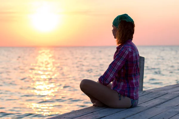 Meisje doet yoga asana op een oude houten pier en geniet van de zonsondergang op de zee — Stockfoto