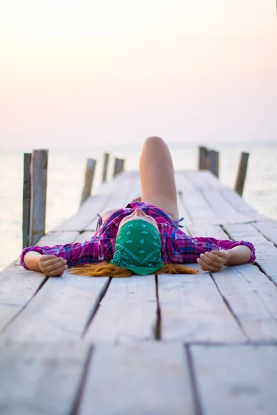 Девушка лежит на старом деревянном пирсе и наслаждается теплым вечером — стоковое фото