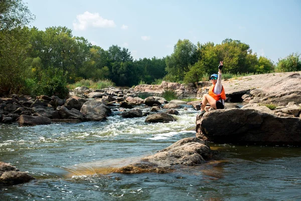 Frau mit Mütze sitzt auf dem großen Stein über dem Wildwasserfluss — Stockfoto