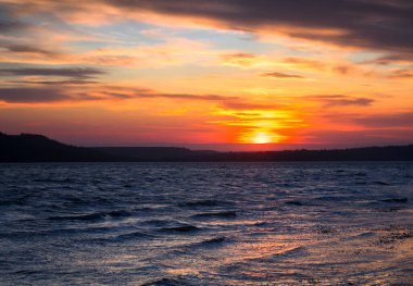 Küçük dalgalarla gölün üzerinde turuncu ve mavi gün batımı