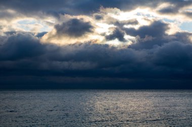 blue dark stormy clouds above the sea, the sunlight breaks through the clouds