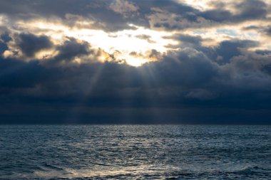 blue dark stormy clouds above the sea, the sun rays breaks through the clouds
