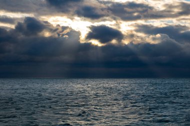 blue dark stormy clouds above the sea, the sun rays breaks through the clouds