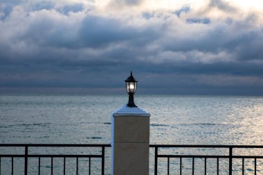 a lantern on the fence of the embankment is on, sea and stormy clouds on the background