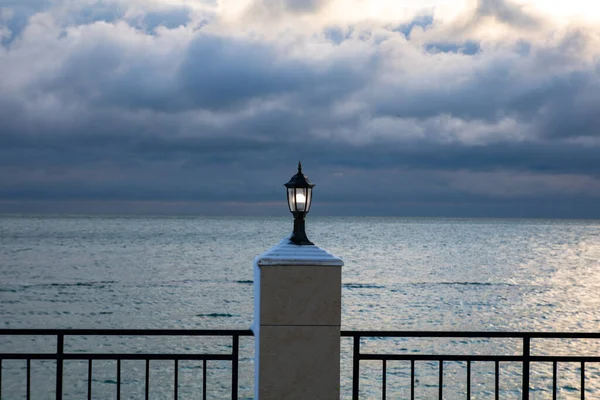 Lucerna na plotu na nábřeží je zapnutá, moře a bouřlivé mraky na pozadí — Stock fotografie
