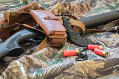 close-up view of black hunting shotgun and karambit knife on the camouflage background