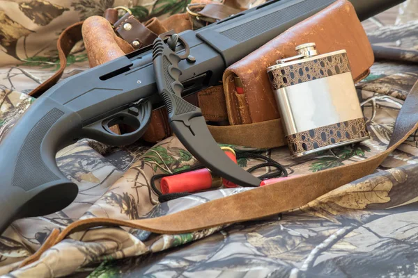 Vista de cerca del frasco, cuchillo de karambit y cinturón de cartucho. escopeta de caza negro y camuflaje en el fondo — Foto de Stock