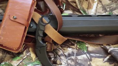 close-up view of black hunting shotgun and karambit knife on the camouflage background