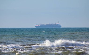 Ufukta büyük bir kargo gemisi, ön planda küçük dalgalar.