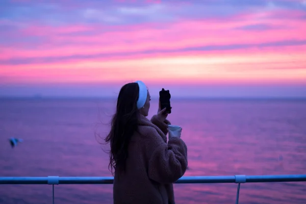 Молодая Девушка Шубе Чашкой Кофе Фотографирует Набережной Живописный Красный Восход — стоковое фото