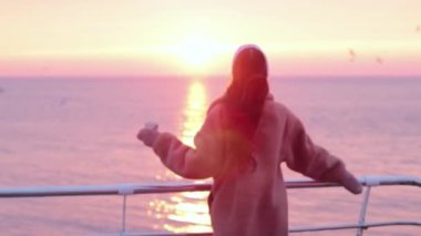 Deniz kenarında kahve fincanı taşıyan kürklü genç kız güzel bir gün doğumu görmekten mutlu.