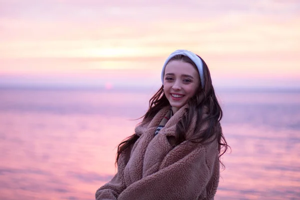 一个穿着毛皮大衣的可爱的小女孩看到海上的红色日出 面带微笑 很高兴 — 图库照片
