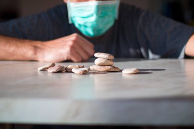 Tıbbi maskeli adam taştan piramit yapıyor ve iyileşmeyi bekliyor.