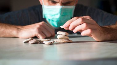 Tıbbi maskeli adam taştan piramit yapıyor ve iyileşmeyi bekliyor.