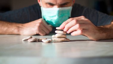 Tıbbi maskeli adam taştan piramit yapıyor ve iyileşmeyi bekliyor.