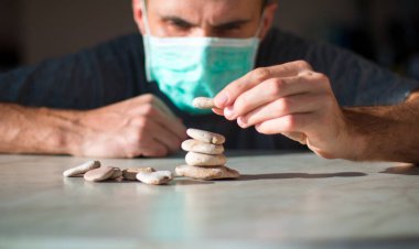 Tıbbi maskeli adam taştan piramit yapıyor ve iyileşmeyi bekliyor.