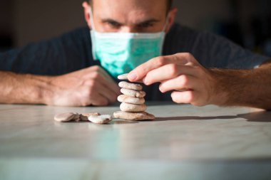 Tıbbi maskeli adam taştan piramit yapıyor ve iyileşmeyi bekliyor.