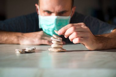 Tıbbi maskeli adam taştan piramit yapıyor ve iyileşmeyi bekliyor.