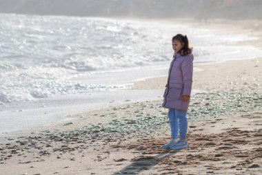 Beyaz ceketli küçük bir kız denize bakıyor.