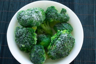 Beyaz tabaktaki donmuş yeşil brokoli ve siyah bambu ahşap arka plan.