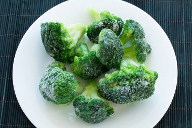 Beyaz tabakta donmuş yeşil brokoli ve siyah bambu ahşap zemin