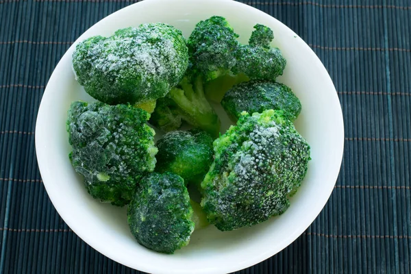Beyaz tabaktaki donmuş yeşil brokoli ve siyah bambu ahşap arka plan.
