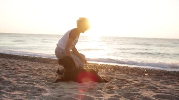 波状の白人女性が日の出の光でビーチでチョコレートラブラドールと遊ぶ — ストック動画